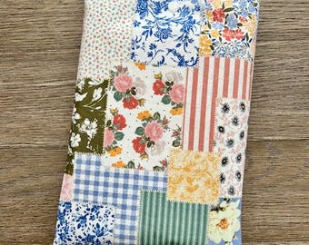May include: A patchwork fabric pouch with a variety of floral patterns in shades of blue, pink, yellow, and green. The pouch is made of cotton and has a quilted texture.