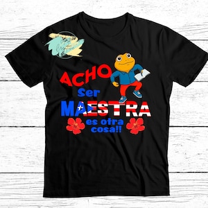 May include: Black t-shirt with the text "Acho Ser Maestra es otra cosa!!" and a cartoon frog wearing a blue shirt and red pants. The word "Maestra" is in the colors of the Puerto Rican flag.