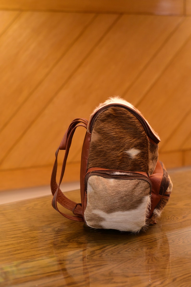 May include: A brown leather backpack with a fur-covered front panel. The fur is a mix of brown and white.