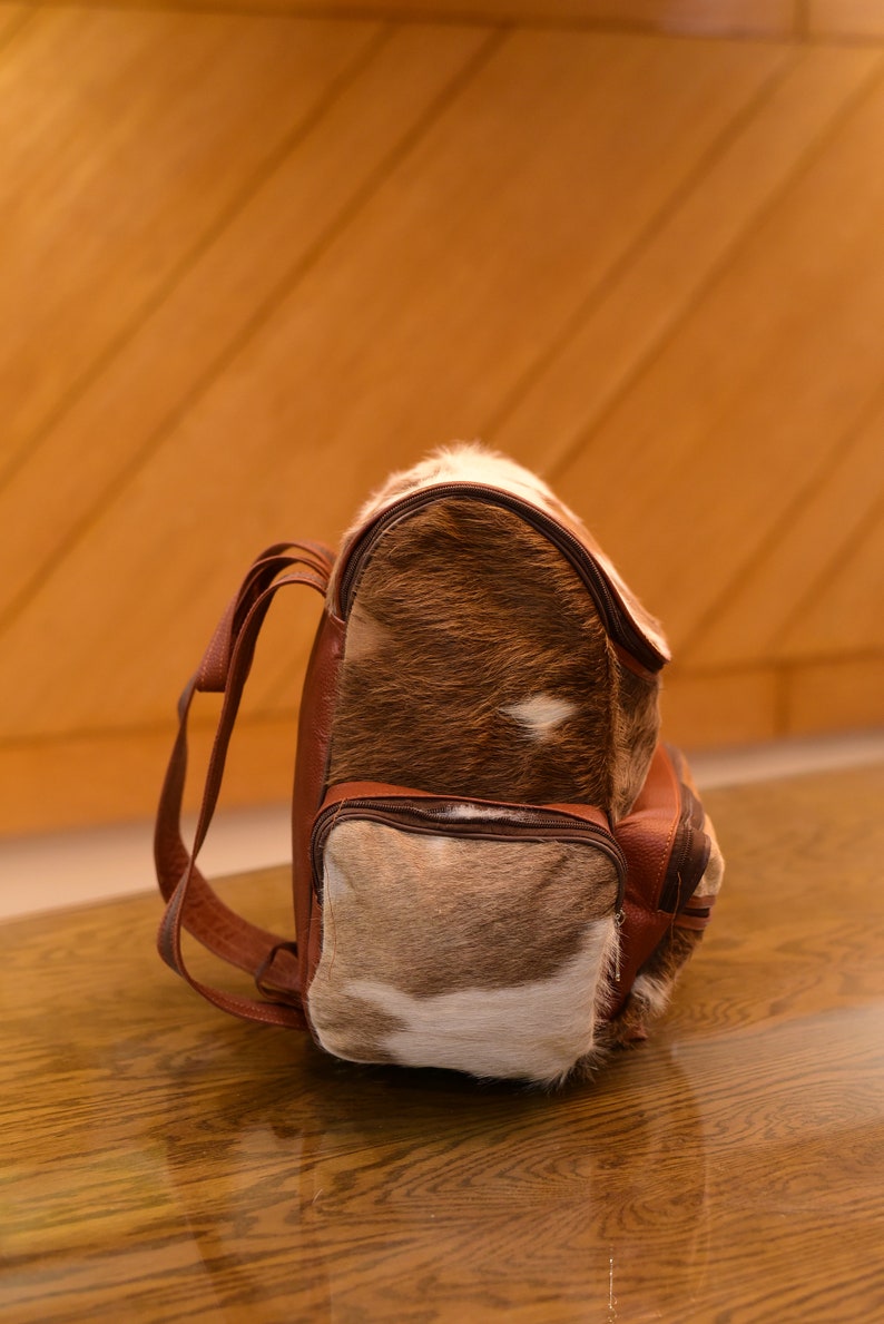 May include: A brown leather backpack with a unique spotted pattern. The backpack has a front pocket and two adjustable straps.