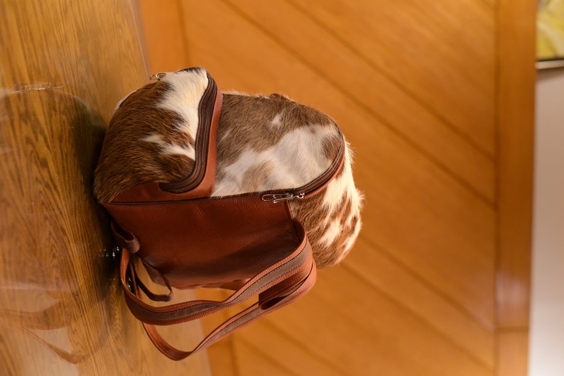 May include: A brown leather backpack with a cowhide pattern. The backpack has a zipper closure and adjustable straps.