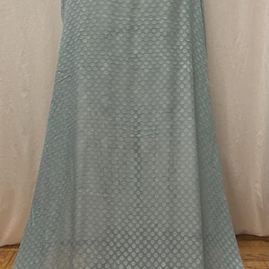 May include: Light blue fabric with a repeating dot pattern. The fabric is draped over a mannequin, showcasing its flow and texture. The material appears soft and lightweight, suitable for apparel or home decor.