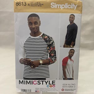 May include: Simplicity sewing pattern 8613 features a man modeling three different shirt styles. The pattern includes a striped shirt with floral sleeves, a black Henley shirt, and a red and gray baseball style shirt. The pattern is from Mimi G Style.