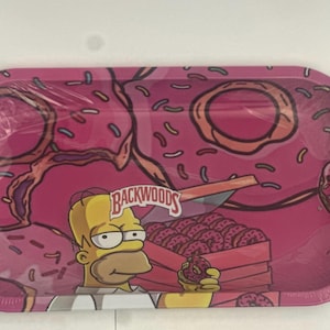 May include: Pink, oval-shaped rolling tray with a cartoon design. The tray features a repeating pattern of pink donuts with sprinkles. The tray also has a cartoon image of Homer Simpson holding a donut, and the text "Backwoods".