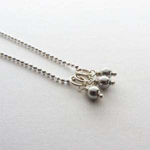 May include: A silver chain necklace with three gray pearl charms hanging from it.