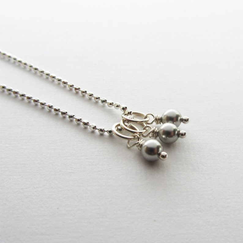 May include: A silver chain necklace with three gray pearl charms hanging from it.