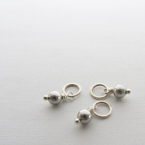 May include: Three silver bead charms with a small loop for attaching to jewelry or other crafts. Each charm features a silver bead with a gray pearl.