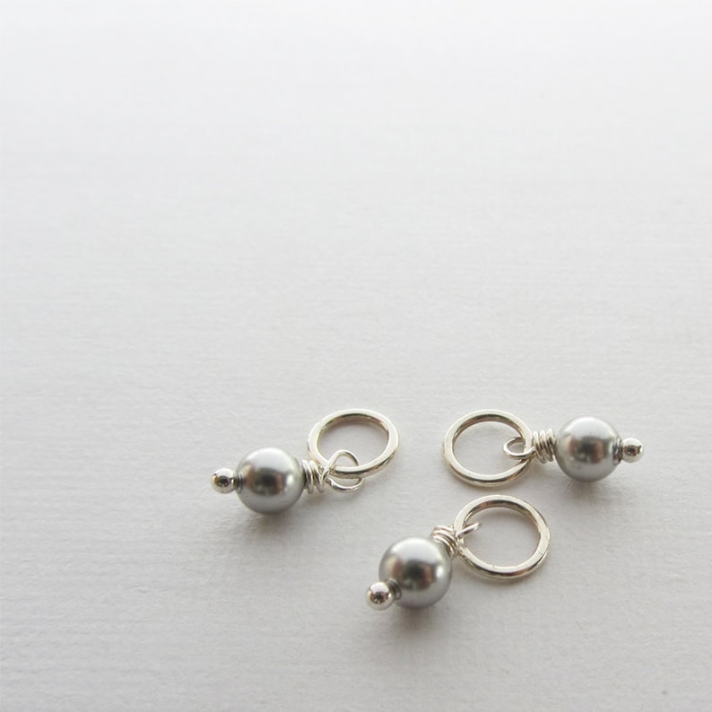 May include: Three silver bead charms with a small loop for attaching to jewelry or other crafts. Each charm features a silver bead with a gray pearl.