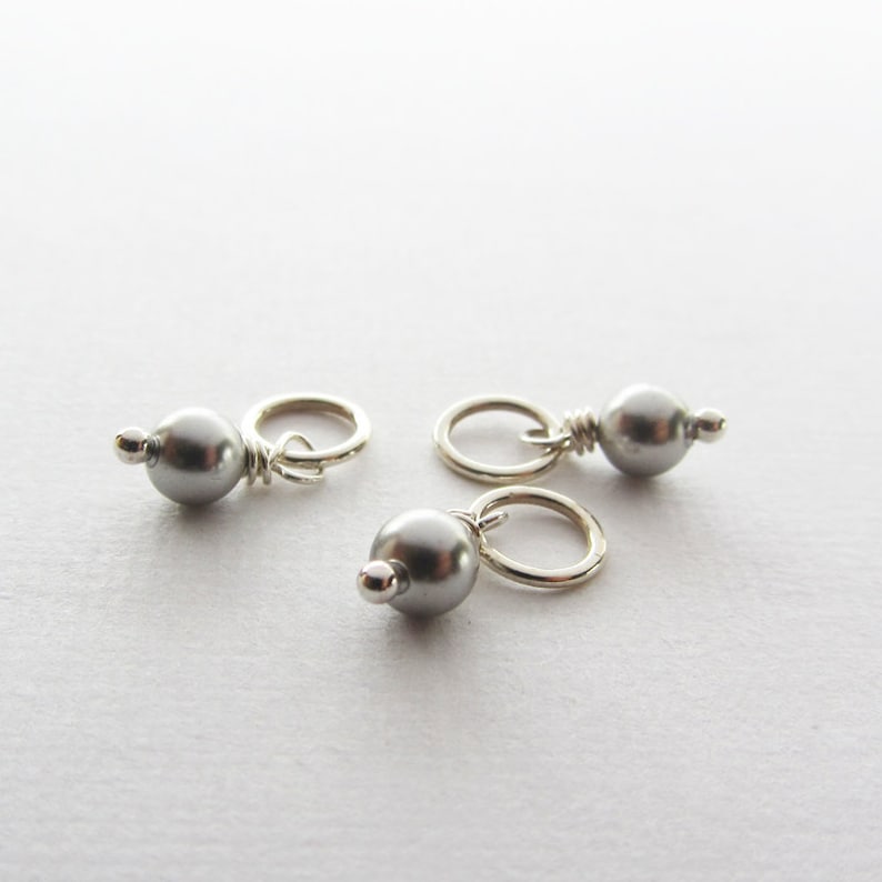 May include: Three silver-toned charms with a small gray pearl attached to each. The charms are designed to be added to necklaces, bracelets, or other jewelry.