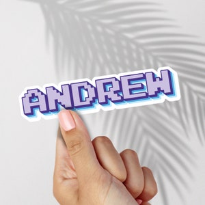 May include: A sticker with the name "ANDREW" in a pixelated font. The letters are light purple with a blue outline and a white background.