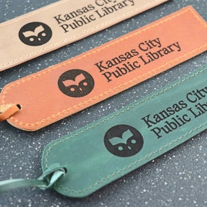May include: Three leather bookmarks with the Kansas City Public Library logo and text. The bookmarks are in brown, orange, and green.
