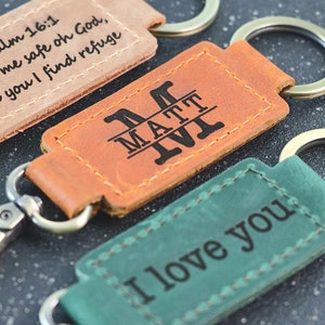 May include: Three leather keychains with different engravings. The first keychain is brown and says "Psalm 16:1 Keep me safe oh God, in you I find refuge". The second keychain is brown and says "MATT VI". The third keychain is green and says "I love you".