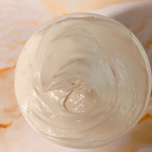 May include: A close-up of a white, creamy substance in a container. The substance is smooth and has a swirl pattern.
