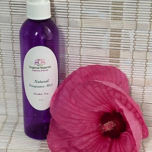 May include: A purple fragrance mist bottle with a white spray top and a pink flower. The bottle has a white label with the text "Inspired Naturals" and "Natural Fragrance Mist". The flower is a vibrant pink.