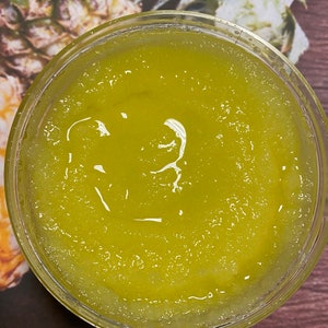 May include: A clear glass jar filled with a yellow-green sugar scrub. The scrub has a grainy texture and is topped with a layer of clear liquid.