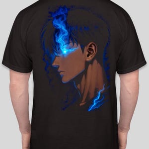 以下が含まれることがあります： 黒いTシャツ。デジタルイラストで、人物の横顔が描かれています。青く光る目と炎のような青いアクセントが特徴です。暗い背景にデザインされ、キャラクターの顔と首が強調されています。