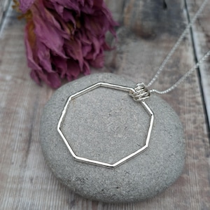 Puede incluir: Un collar de plata con un colgante octogonal. El colgante es una forma geométrica simple con un acabado liso y pulido.