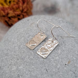 Puede incluir: Un par de pendientes de plata con textura martillada y un diseño en forma de corazón.