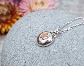 May include: A silver necklace with a round pendant featuring a copper star. The pendant is textured and has a hammered finish.