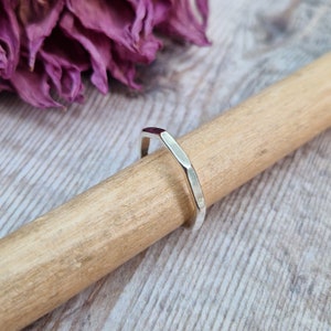 May include: A silver ring with a hexagonal shape. The ring is lying on a wooden surface.