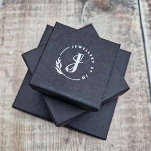 May include: Three black square boxes stacked on top of each other. The top box has a white logo with the text "Jewellery by Jo" and a stylized letter "J" with a leaf design.