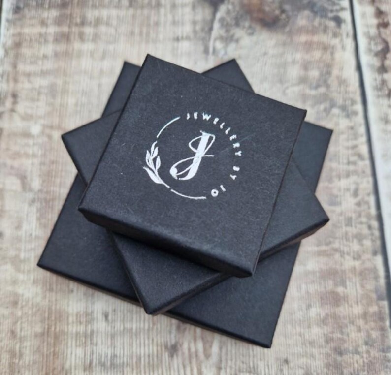 May include: Three black square boxes stacked on top of each other. The top box has a white logo with the text "Jewellery by Jo" and a stylized letter "J" with a leaf design.