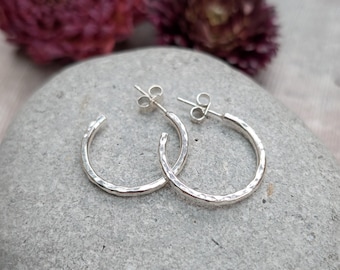 May include: A pair of silver hoop earrings with a hammered texture. The earrings are simple and elegant, and would make a great gift for any occasion.