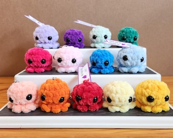 May include: A collection of thirteen small, plush, crocheted octopus toys in various solid colors including pink, orange, red, yellow, blue, purple, and green. Each octopus features two large black plastic eyes and a textured, soft yarn surface.