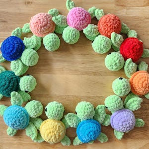 May include: A circle of crocheted sea turtles in various colors, including blue, green, pink, orange, and red. The turtles are arranged in a circle on a wooden surface.