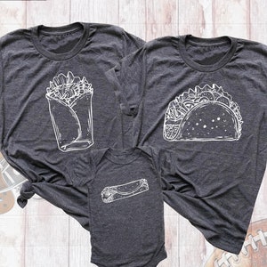 May include: Three gray t-shirts with white outlines of different Mexican food items. The largest shirt has a taco, the medium shirt has a burrito, and the smallest shirt has a rolled-up taco.