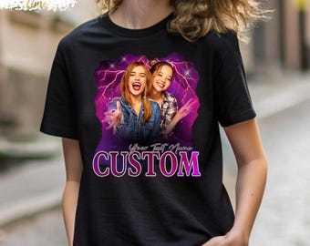 May include: A black short-sleeved t-shirt featuring a graphic print of two smiling individuals against a purple lightning background. Below the image, the text reads Your Text Name CUSTOM in a bold, pink-outlined font style.