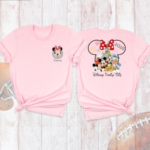 Puede incluir: Dos camisetas de color rosa claro. Una presenta un gr&aacute;fico de Minnie Mouse con la palabra "Custom" debajo. La otra camiseta tiene un dise&ntilde;o de oreja de Mickey Mouse con "2025" y un grupo de personajes de Disney, con las palabras "Disney Family Trip".