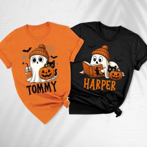 May include: An orange t-shirt with a ghost wearing a beanie, holding a drink, and a black cat with a pumpkin, labelled TOMMY. A black t-shirt with a ghost reading a book, a black cat, and a pumpkin, labelled HARPER, both featuring bats.