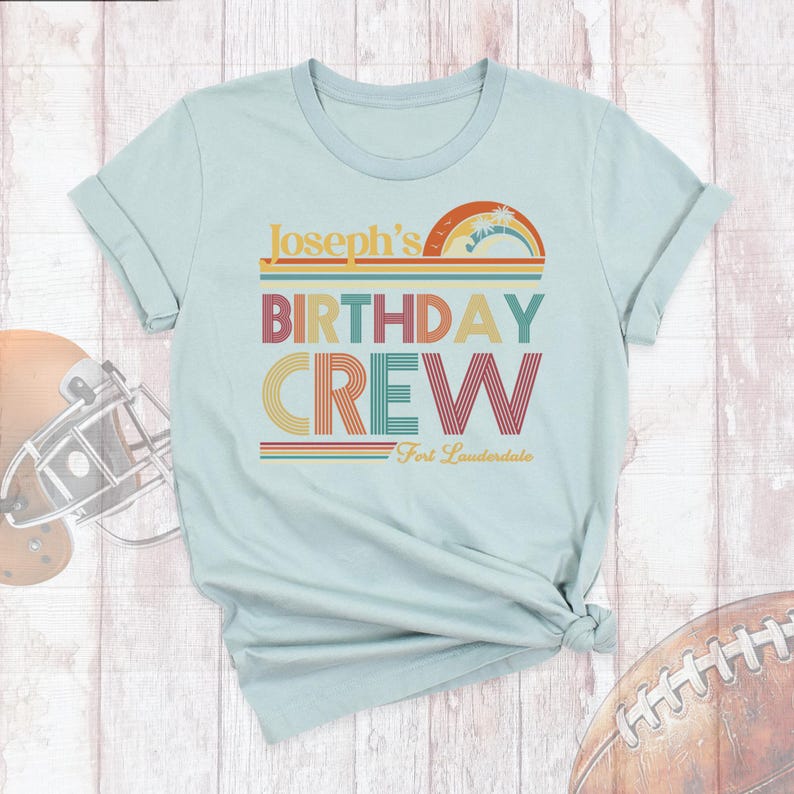 May include: Light blue t-shirt with a retro-style design that says "Joseph's Birthday Crew" with a rainbow and stripes. The text "Fort Lauderdale" is below the main text.