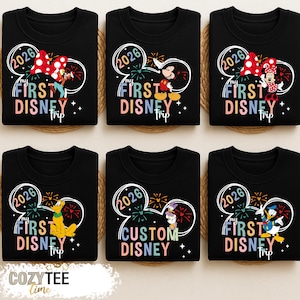Puede incluir: Sudaderas negras con dise&ntilde;os de personajes de Disney. Cada camiseta presenta un contorno de oreja de Mickey Mouse con el texto "2026" y "My First Disney Trip". Los personajes incluyen a Mickey, Minnie, Pluto, Donald Duck y Daisy.