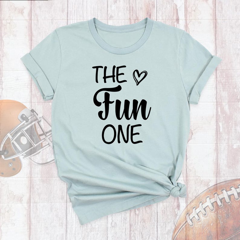 May include: A light blue t-shirt with the text "THE &hearts; Fun ONE" printed in black.