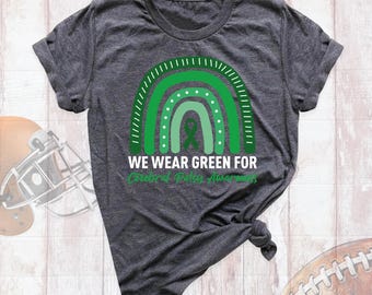 May include: A dark heather gray short-sleeve t-shirt featuring a green rainbow graphic with a central awareness ribbon. The text reads WE WEAR GREEN FOR Cerebral Palsy Awareness in white and green lettering across the chest area.
