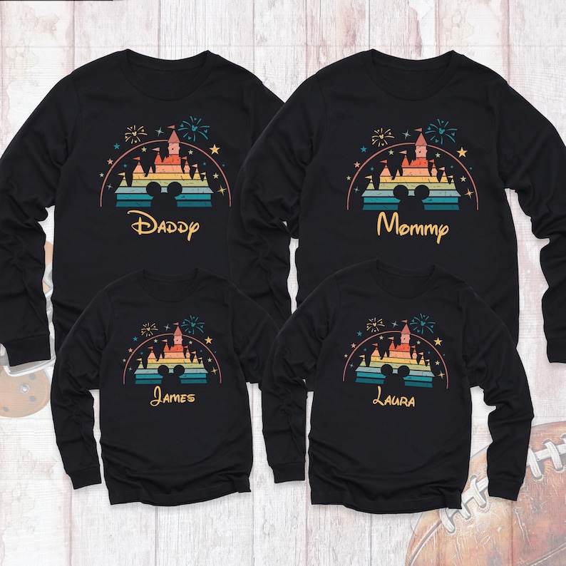 May include: Four black long-sleeved shirts with a retro-style graphic of a castle with fireworks and the text "Daddy", "Mommy", "James", and "Laura".