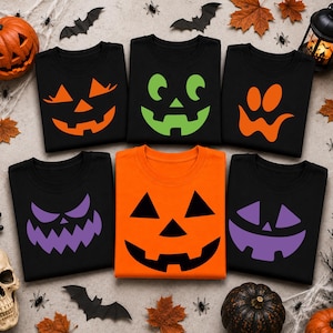 May include: Five black t-shirts and one orange t-shirt, each featuring a unique jack-o'-lantern face graphic. The designs include orange, green, and purple facial features printed on the shirts, arranged in a grid pattern.