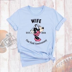 Puede incluir: Camiseta azul claro con el texto "Wife Est. 2024 Our First Anniversary" y una imagen de dibujos animados de Minnie Mouse.