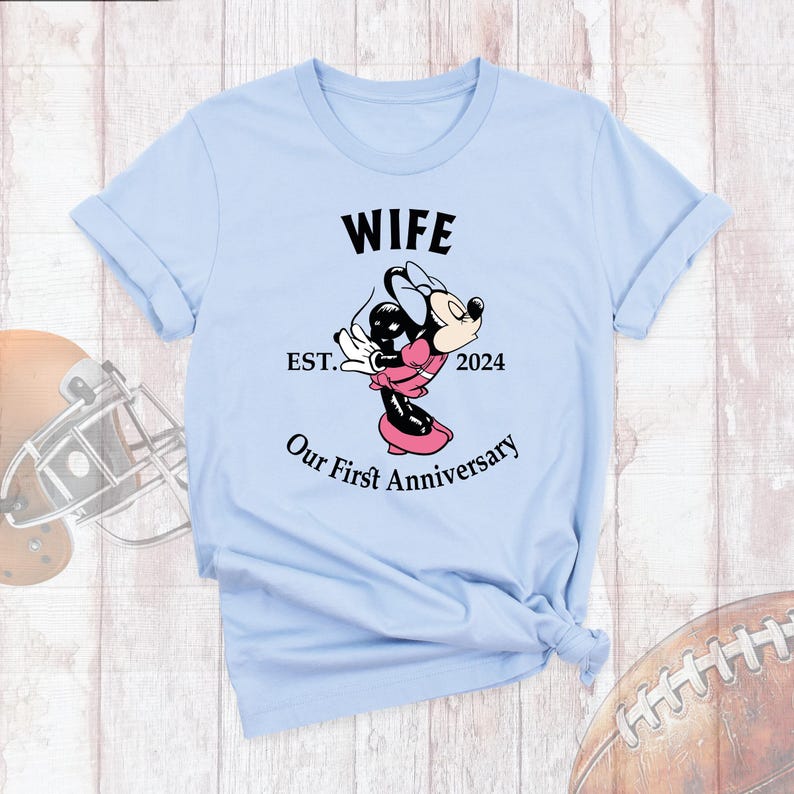 Puede incluir: Camiseta azul claro con el texto "Wife Est. 2024 Our First Anniversary" y una imagen de dibujos animados de Minnie Mouse.