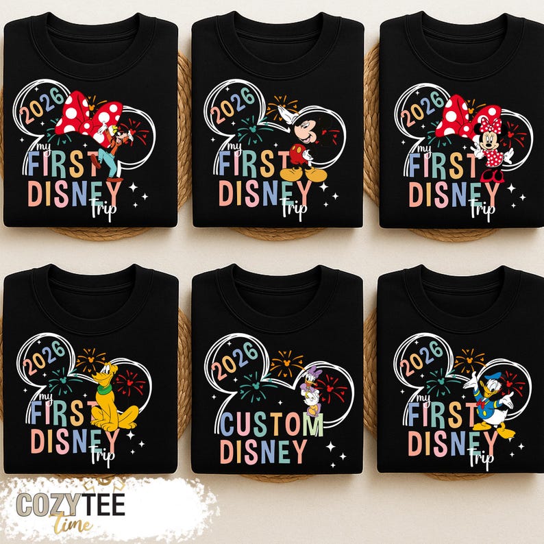 Puede incluir: Sudaderas negras con dise&ntilde;os de personajes de Disney. Cada camiseta presenta un contorno de oreja de Mickey Mouse con el texto "2026" y "My First Disney Trip". Los personajes incluyen a Mickey, Minnie, Pluto, Donald Duck y Daisy.