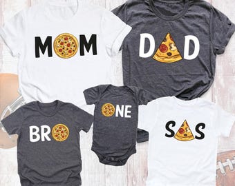 May include: A set of five shirts and a bodysuit featuring pizza-themed graphics. The white shirts display the words MOM and SOS with pizza slices, while the dark gray shirts feature DAD, BRO, and ONE with pizza slice illustrations.