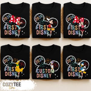 Puede incluir: Sudaderas negras con dise&ntilde;os de personajes de Disney. Cada camiseta presenta un contorno de oreja de Mickey Mouse con el texto "2026" y "My First Disney Trip". Se representan varios personajes de Disney, incluidos Mickey, Minnie, Pluto y Donald Duck.