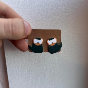 May include: A pair of green and white teapot earrings on a brown card. The teapots have a white lid and a brown spout.