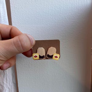 May include: A pair of tea bag earrings on a brown card. The earrings are made of polymer clay and are shaped like tea bags. The tea bags are beige with a red "tea" label and a black string.
