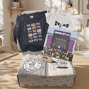 May include: A gift box containing a dark gray sweatshirt with a cassette tape print, a white baby bodysuit with a clothesline graphic, a gray t-shirt with a skeleton hand and rose graphic reading IT WAS NEVER A PHASE, and a book titled GROWING UP EMO.