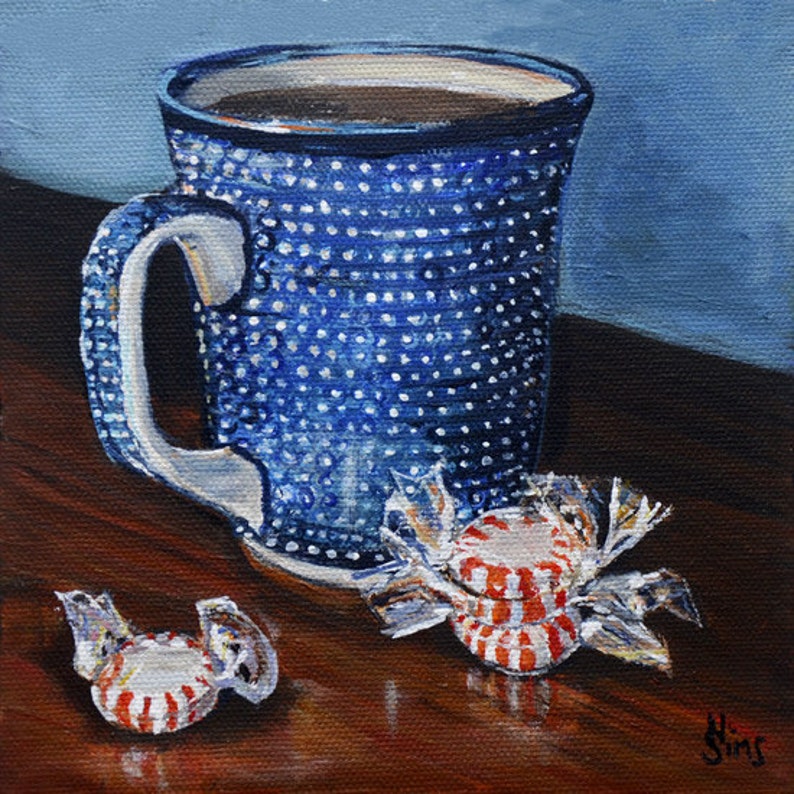Puede incluir: Una taza azul y blanca con lunares con caf&eacute; y dos caramelos rojos y blancos a rayas sobre una mesa de madera.