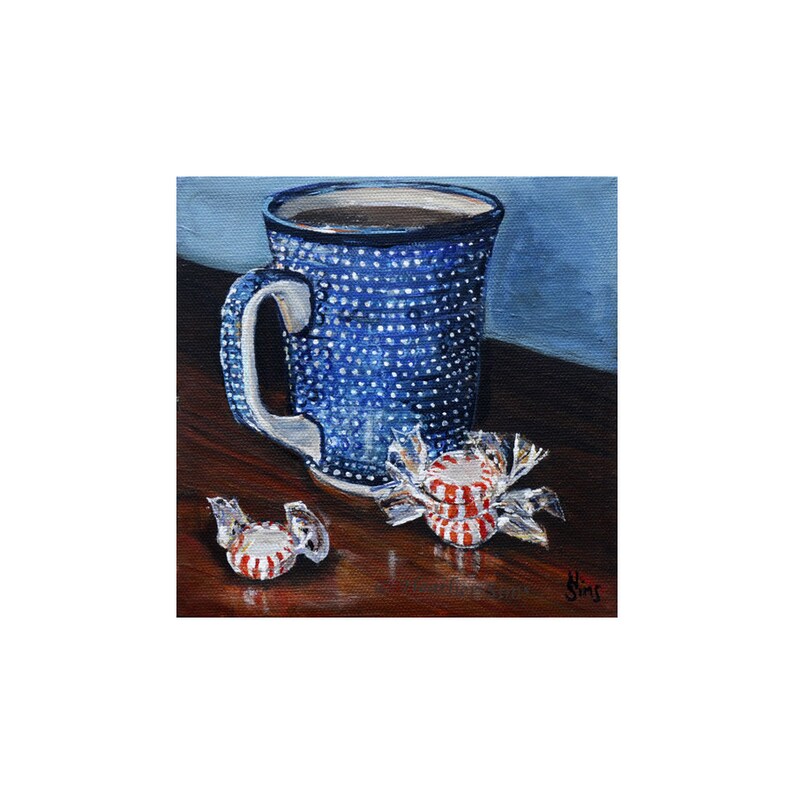 Puede incluir: Una taza azul y blanca con lunares llena de caf&eacute; se encuentra sobre una superficie de madera junto a tres caramelos de menta roja y blanca.