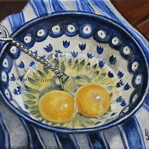 May include: Two raw egg yolks in a blue and white patterned bowl with a silver spoon. The bowl is on a blue and white striped cloth.